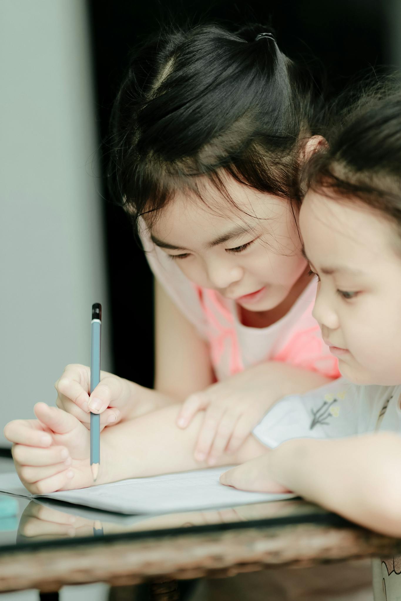 Two young girls focusing on studying together indoors, bonding over a shared activity.